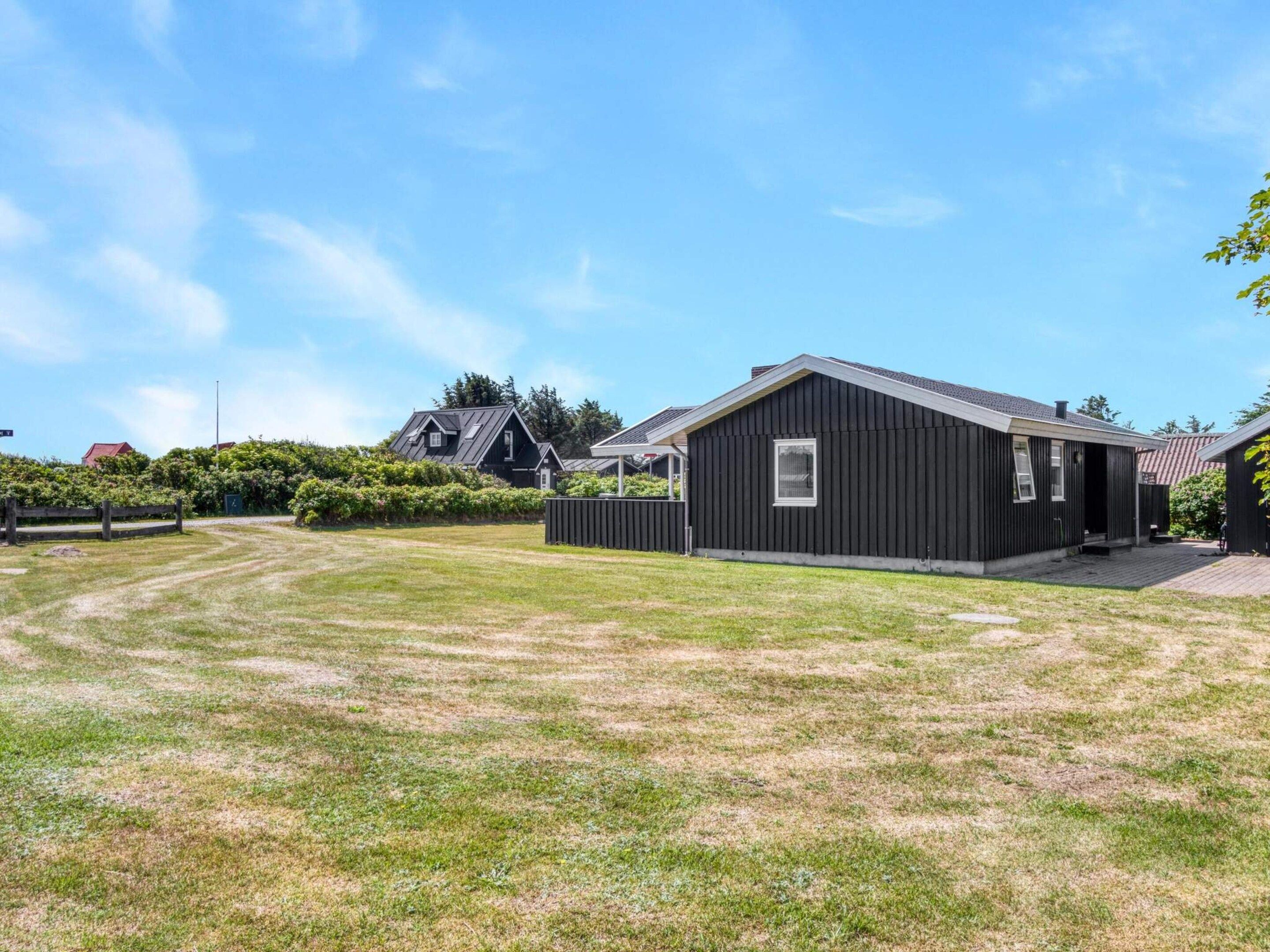 A residential property with a large grassy yard, a black building, and a red-roofed house in the background.