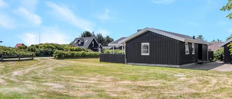 A residential property with a large grassy yard, a black building, and a red-roofed house in the background.
