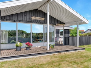 A covered outdoor area with a sign reading 'Miramare,' wooden deck, potted plants, and a view of a garden and pool.