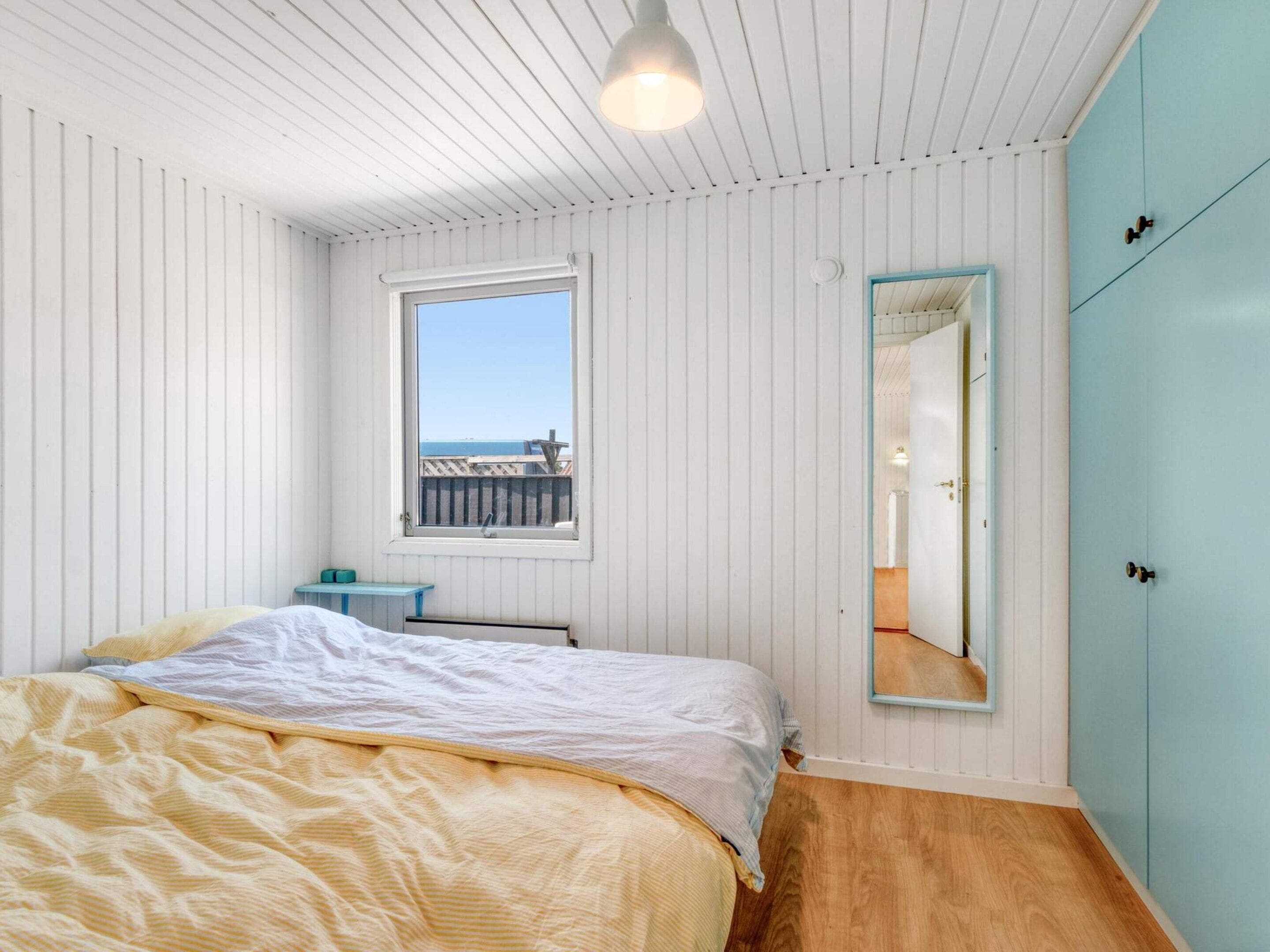 Een slaapkamer met een bed, een raam, een spiegel en een kledingkast.