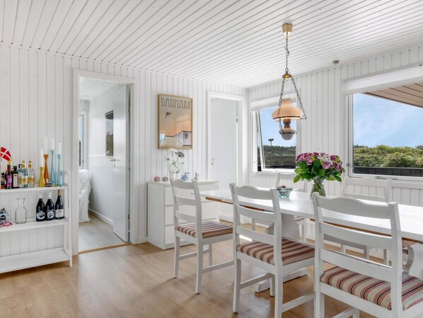 A dining area with white wooden furniture, a hanging light fixture, and a view through a window.