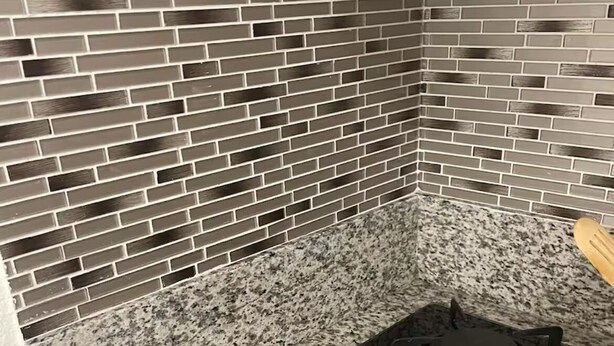 Une cuisine avec un poêle noir, un plan de travail en granit et un pare-feu fait de carreaux gris.