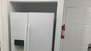 Un réfrigérateur blanc doté d’un distributeur d’eau, une porte blanche et un extincteur fixé au mur.