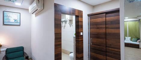 A compact room with a wooden wardrobe, a green chair, a small table, and a wall-mounted air conditioner.