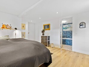 A bedroom with a bed, a dresser, a mirror, and a door leading to a bathroom with a tiled shower. - 5 Star Holiday Home in Lokken (Lokken)