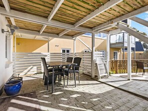 An outdoor patio with a table and chairs, a wooden fence, and a building in the background. - 5 Star Holiday Home in Lokken (Lokken)