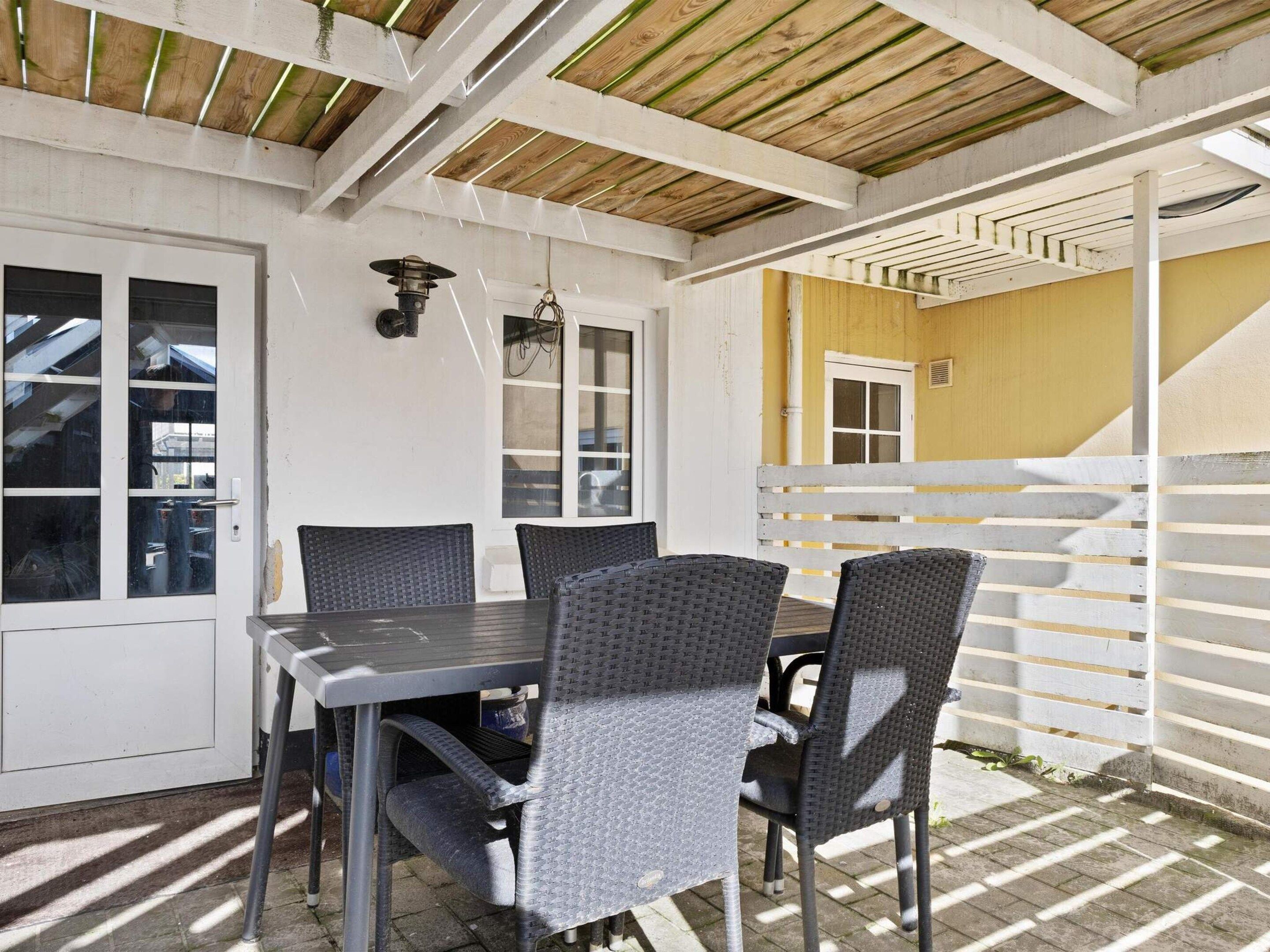 An outdoor patio area with a table and chairs, a wooden ceiling, and a white fence.