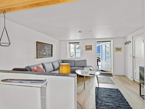 A living room with a sofa, a coffee table, and a lamp. There is a door leading to a balcony.