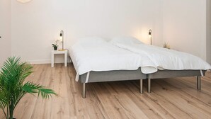 A minimalist bedroom with a bed, bedside tables, and a hanging light fixture. - 2 Person Holiday Home in Ringkobing (Ringkobing)