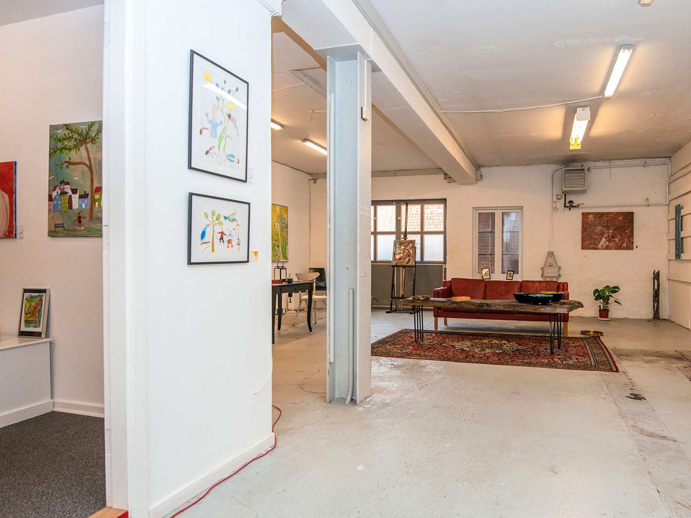 Uma galeria de arte com pinturas nas paredes, um sofá vermelho e uma mesa com uma tigela.