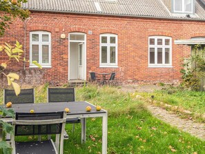 A brick house with a garden, a table with chairs, and a door. - 2 Person Holiday Home in Ringkobing (Ringkobing)