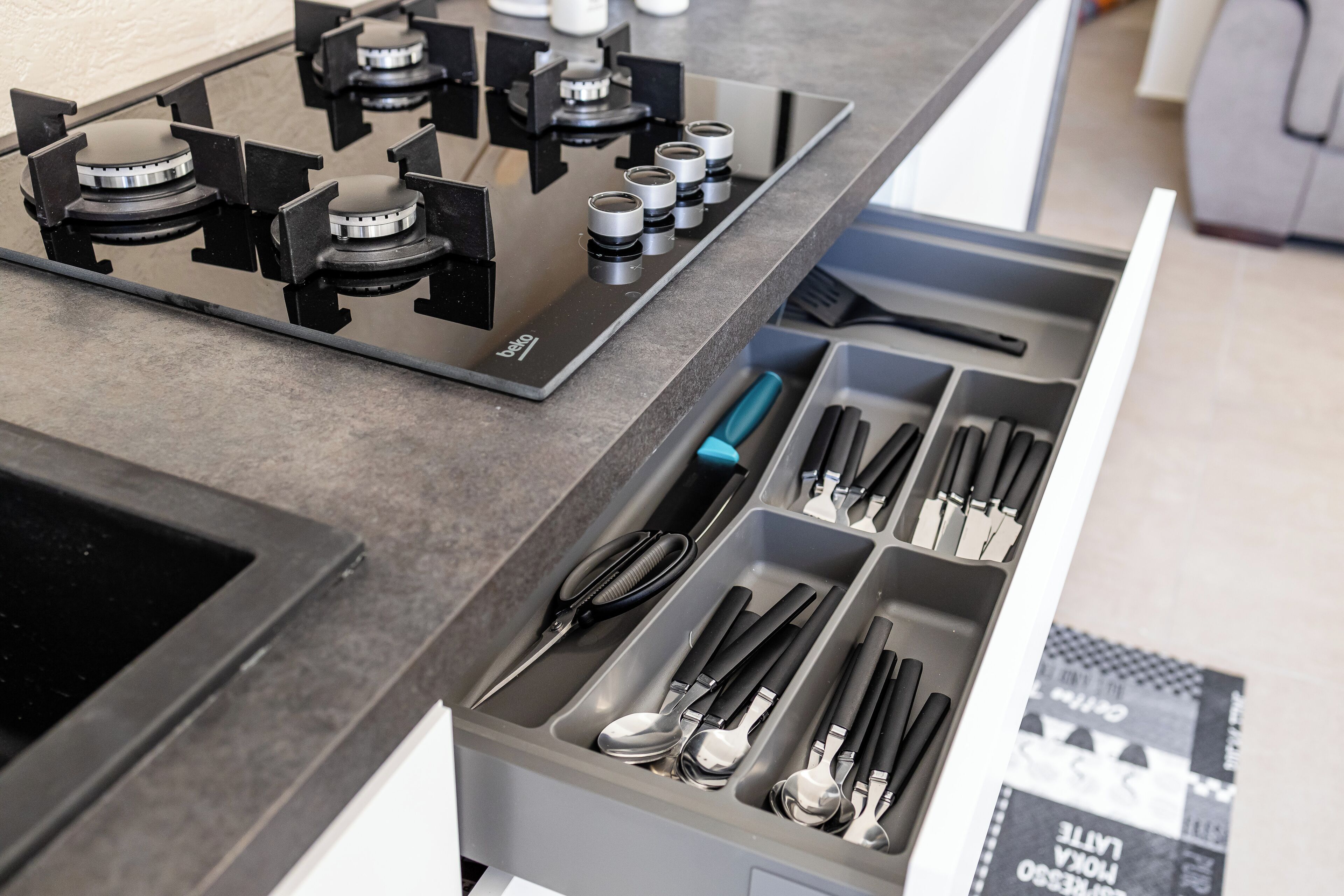 A kitchen with a gas stove and a drawer organizer with utensils.