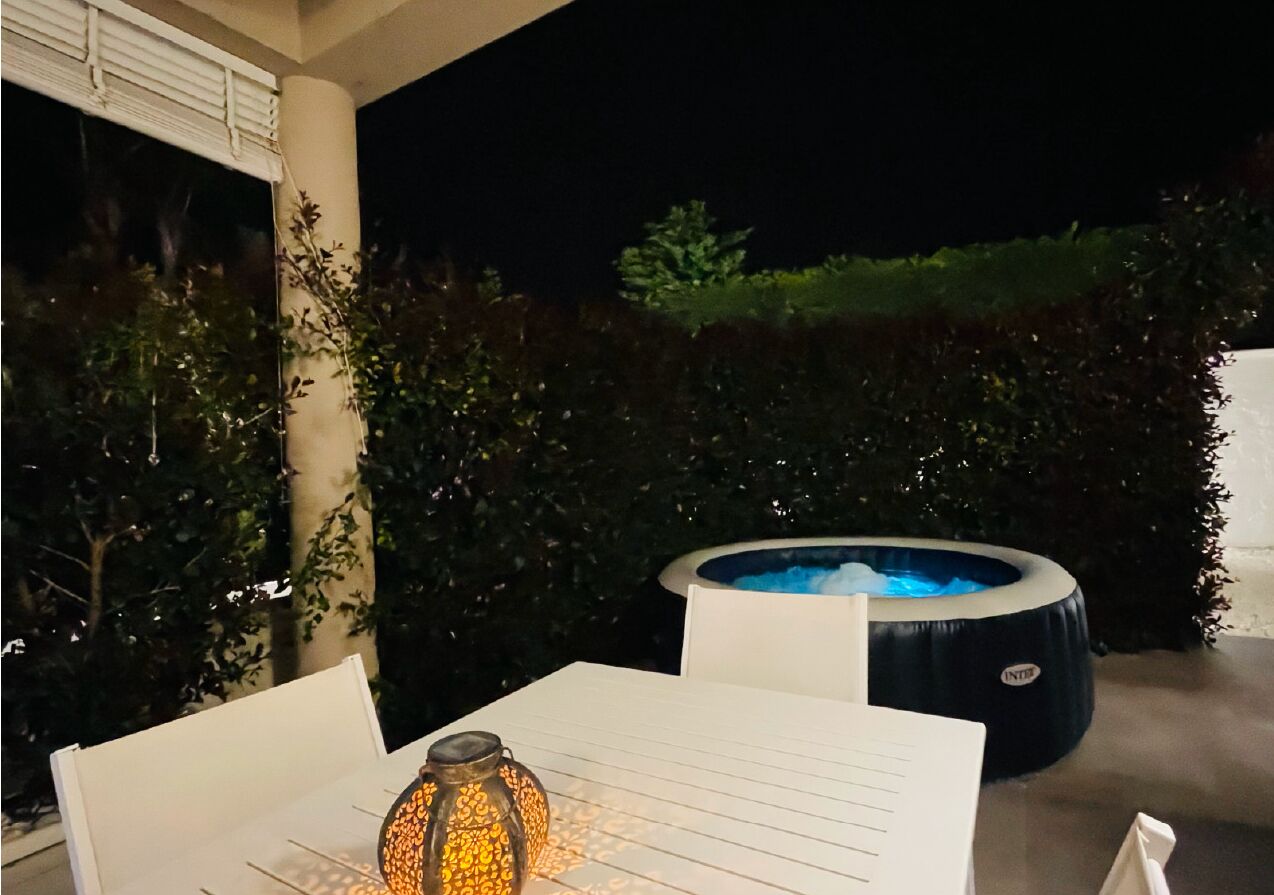 An outdoor seating area with a table, a glass bottle, and a hot tub.