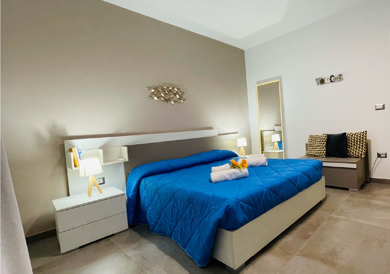A modern hotel room with a large bed, bedside tables with lamps, a mirror, and a desk with a chair.