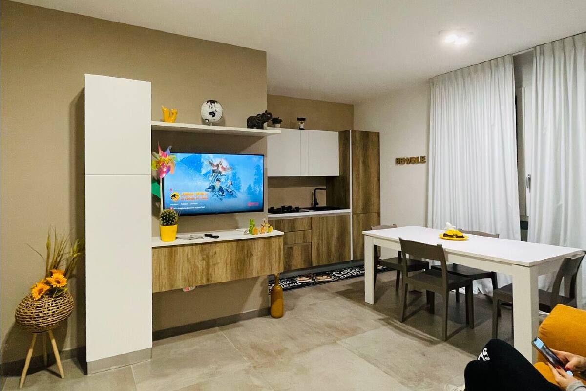 A modern kitchen with a TV, white cabinets, and a dining area with a table and chairs.