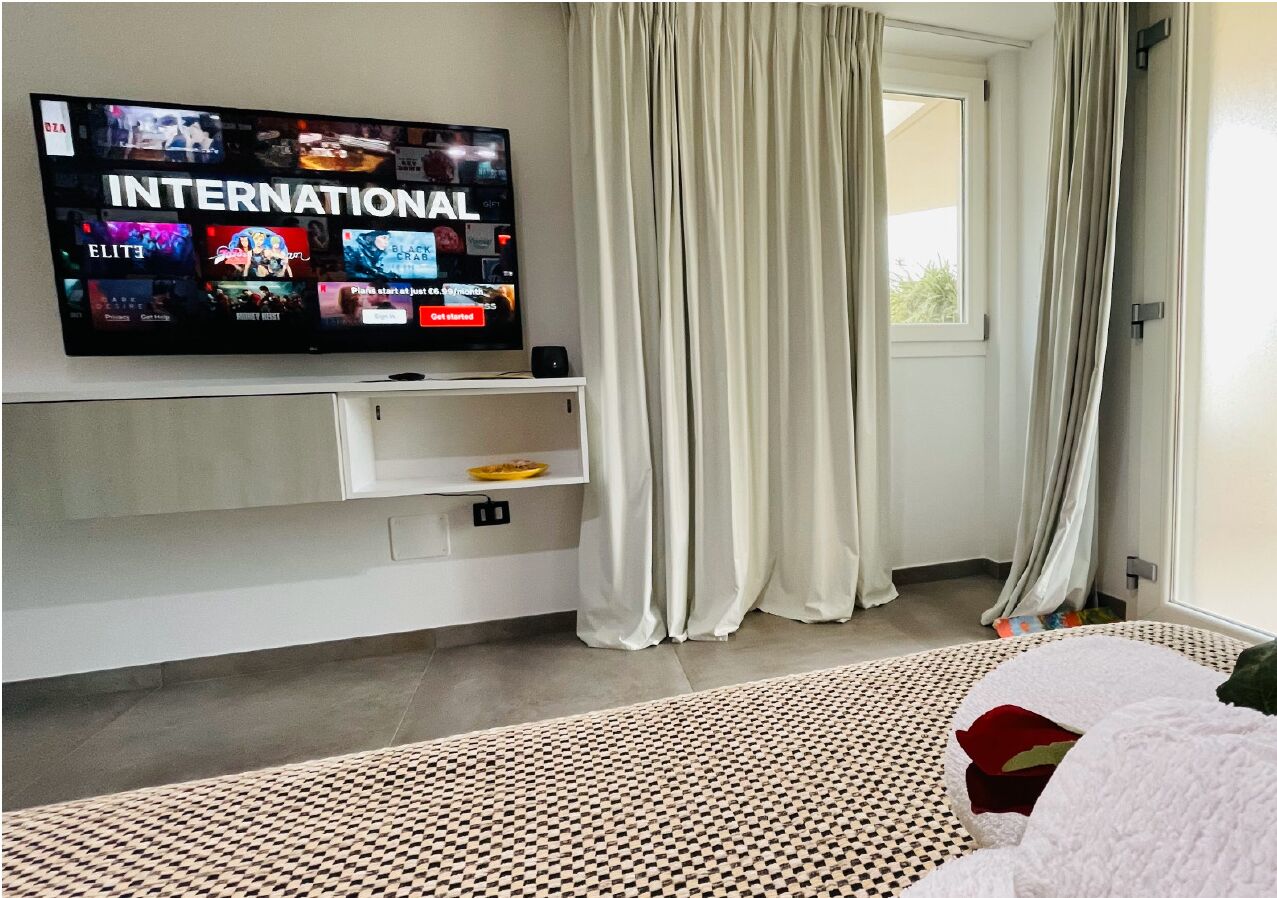Ett hotellrum med en platt-TV som är monterad på väggen och visar en kanal som heter ”INTERNATIONAL”. Under TV:n står ett vitt konsolbord, och på golvet ligger en mönstrad matta.