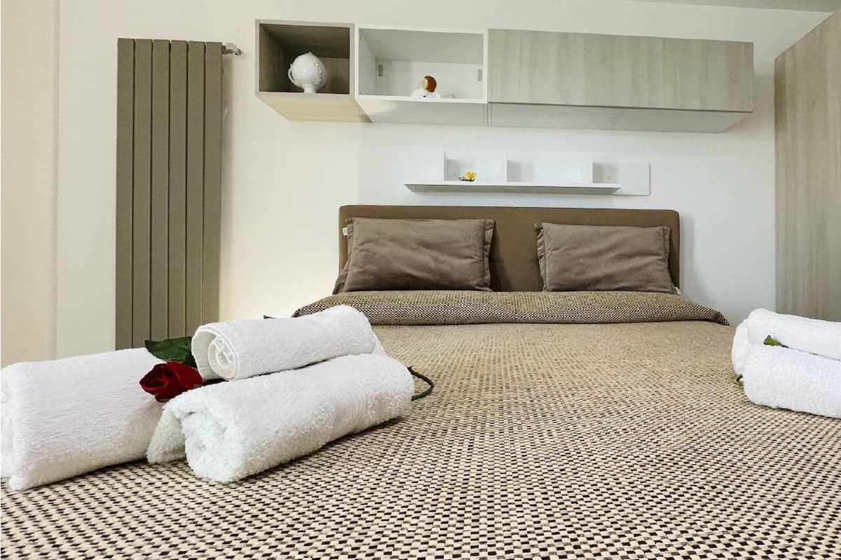 A neatly made bed with a checkered bedspread, two pillows, and rolled white towels with a red rose.