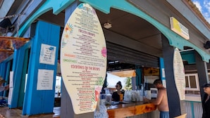 Um bar à beira-mar com um quadro de menu exibindo bebidas e coquetéis.