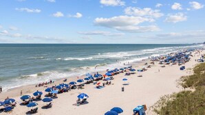 Uma praia com fileiras de guarda-sóis e espreguiçadeiras, areal e o oceano ao fundo.