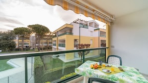Un balcon avec une table préparée pour le petit-déjeuner, donnant sur un immeuble à la façade jaune et une pelouse verte.