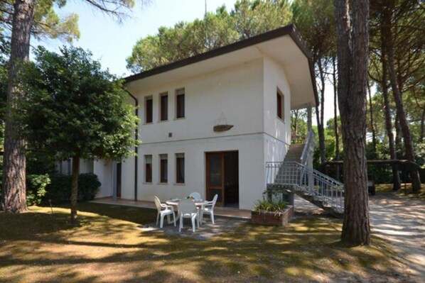 A two-story building with a white exterior, a staircase leading to the upper floor, and a small outdoor seating area with white chairs.