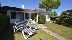 Ein Bungalow mit Terrasse, zwei Liegestühlen, einem kleinen Tisch und einem großen Baum.