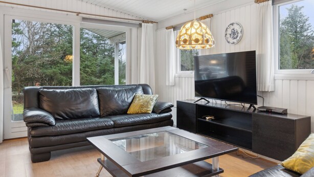 Un salon moderne avec un canapé en cuir, une table basse en verre, un téléviseur à écran plat et un luminaire suspendu.