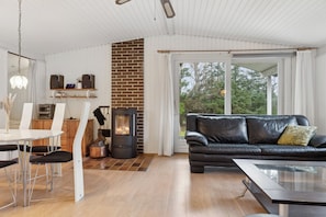 A modern living room with a fireplace, a black leather sofa, a dining table with chairs, and a large window.