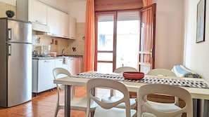 Una cucina compatta con frigorifero, fornello e lavello. C'è un tavolo da pranzo con sedie e una finestra con tende.
