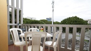 A balcony with a table and four chairs, a potted plant, and a view of the street and buildings. - Flat near the beach and Faro Rosso in Lignano (Lignano Sabbiadoro)