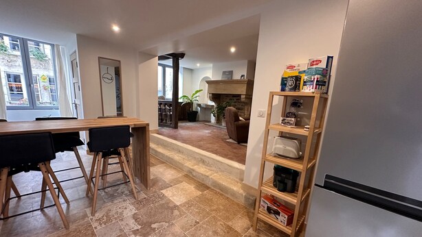 A modern kitchen with a dining area, a built-in bookshelf, and a view of the living room. - Au petit Langres: Downtown accommodation (Langres)