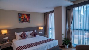 A hotel room with a large bed, two bedside tables, a nightstand, a window with curtains, and a painting on the wall. - Siddhartha Hotel Damauli (Byas)