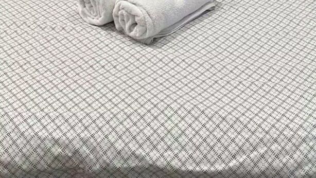 A neatly made bed with a checkered bedspread, two pillows, and two rolled towels.