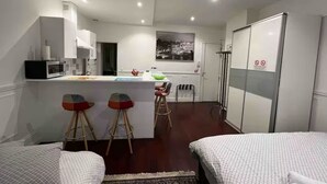 A compact hotel room with a kitchenette, a dining area with stools, a bed, and a large window.