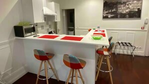 A modern kitchen with a white countertop, two stools, and a cityscape painting on the wall.