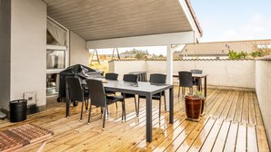 Une terrasse couverte avec une table et des chaises, un barbecue et une plante en pot.