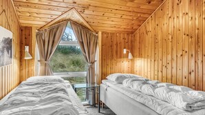 Une chambre dans un chalet en bois, avec deux lits, une fenêtre avec des rideaux et une lampe.