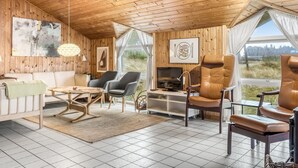 L’intérieur chaleureux d’un chalet avec des murs en bois, un canapé, des fauteuils, un téléviseur et un coin repas.