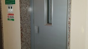 Une porte avec une petite fenêtre, un panneau d’affichage fixé au mur avec des instructions et une prise de courant.