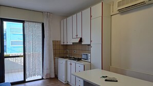 Une cuisine compacte avec des meubles blancs, une cuisinière encastrée et un four à micro-ondes. Une porte-fenêtre coulissante donne accès à un balcon extérieur.