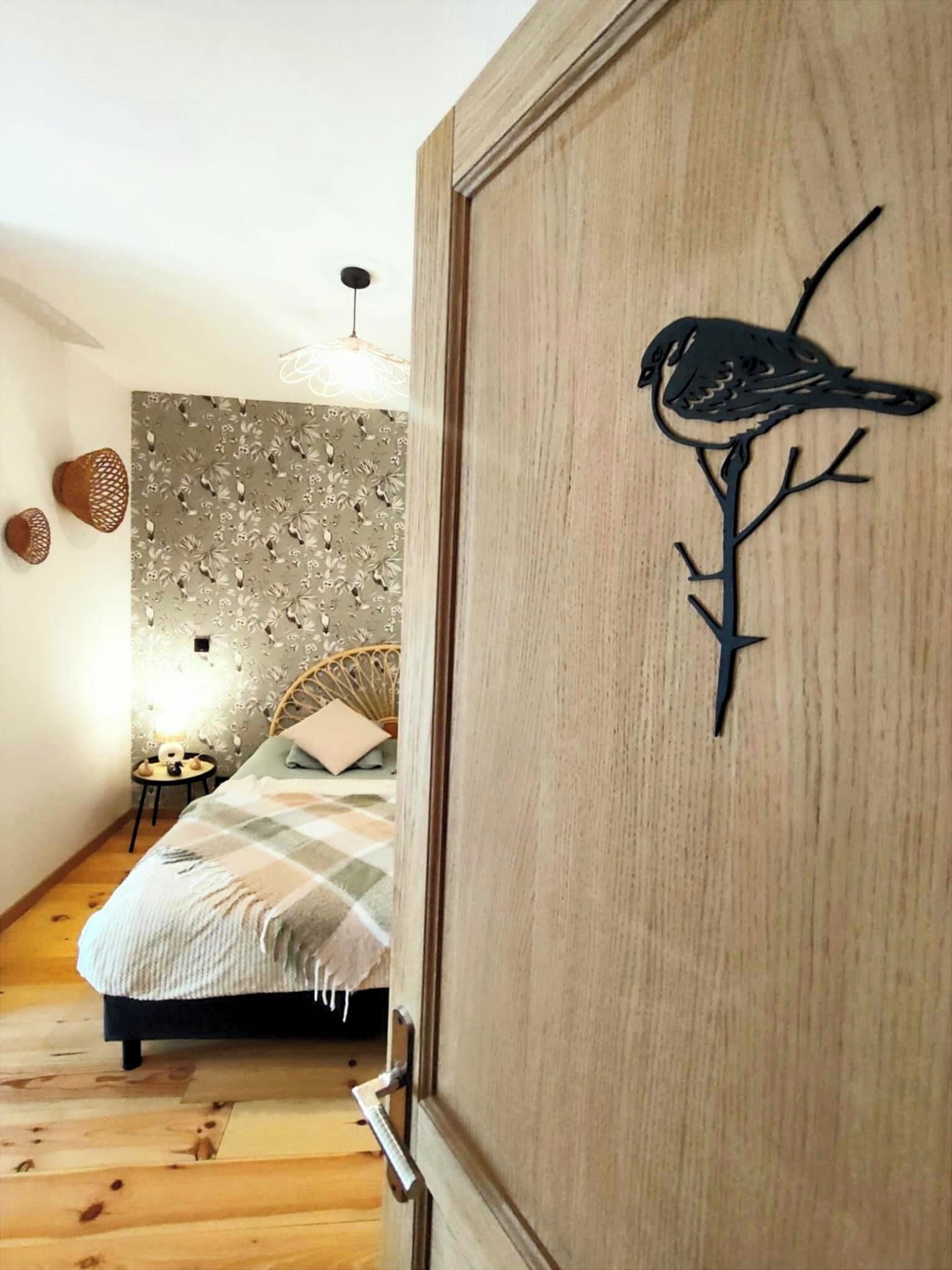 Una camera da letto con un letto, una porta di legno decorata con un intaglio a forma di uccello, una parete con carta da parati floreale e una lampada a sospensione.