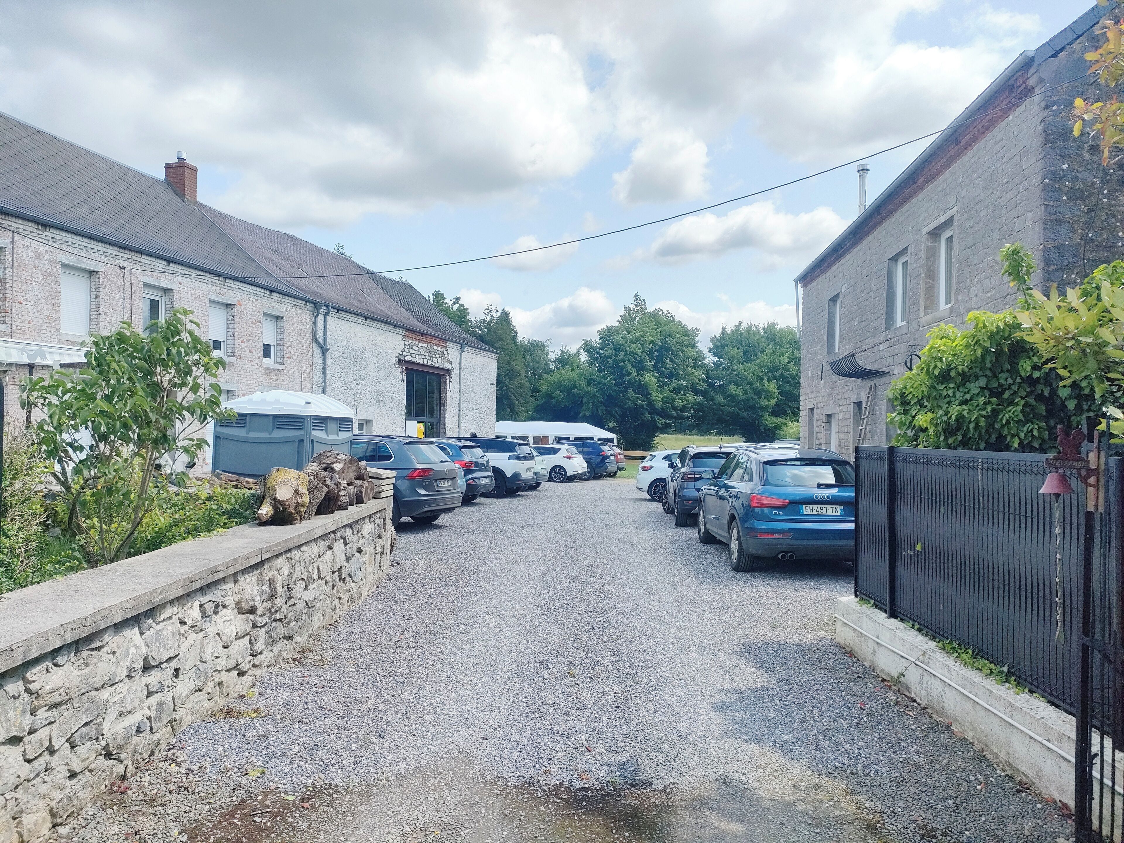 Une allée de gravier mène à une rangée de voitures garées dans un quartier résidentiel, bordé de murs en pierre et de bâtiments en briques.