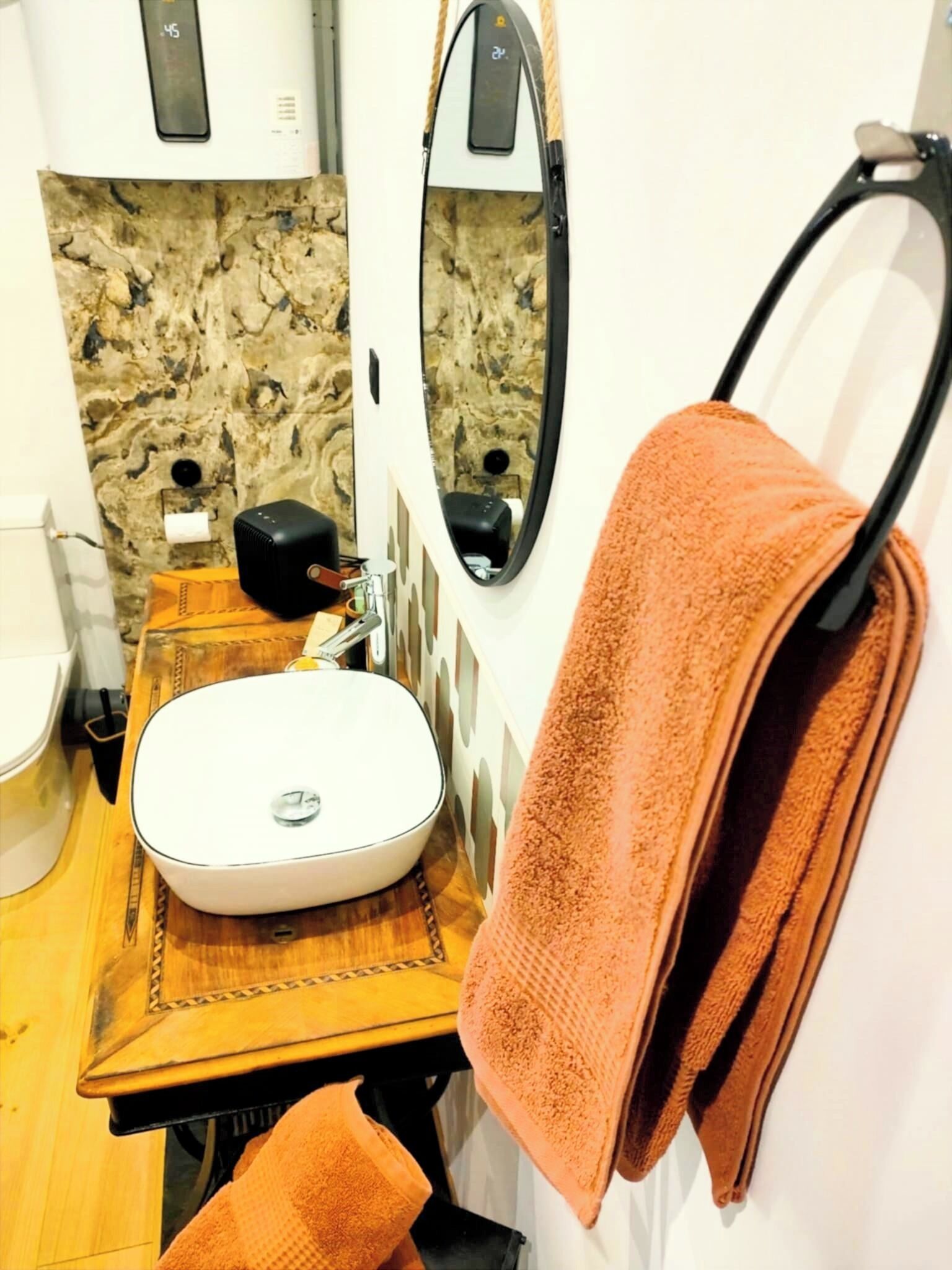 Een badkamer met een witte wastafel, een spiegel, een handdoekrek met een handdoek en een wand met marmerprint.