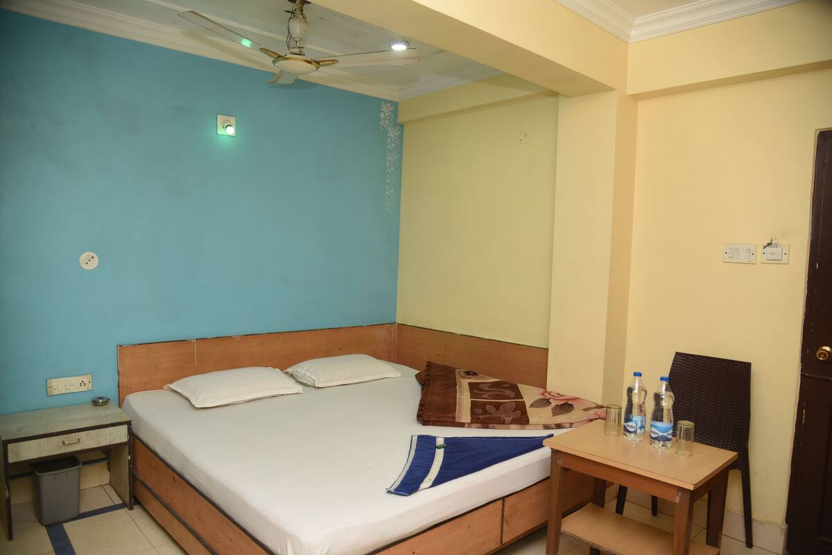 A bedroom with a bed, bedside table, and a small table with water bottles and glasses.