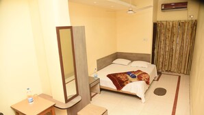 Hotelkamer met een bed, bureau, stoel, spiegel, plafondventilator en airconditioning.