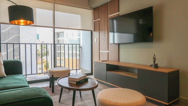A modern living room with a large TV, green sofa, and a balcony with a view of buildings. - w *| Grand 1BR with Great Balcony in San Isidro (San Isidro)