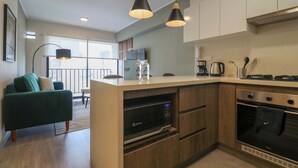 A modern kitchen with a built-in microwave, oven, and coffee maker. There is a dining area with a green sofa and a balcony with a view. - w *| Grand 1BR with Great Balcony in San Isidro (San Isidro)