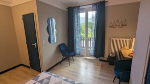 A room with a wooden floor, a blue chair, a table with a hat, a radiator, and a view of greenery outside. - Le Balandri - Double hotel room (Lully)