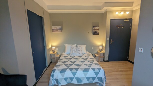 A bedroom with a bed, two bedside tables, a door, and a wall-mounted light fixture. - Le Balandri - Double hotel room (Lully)
