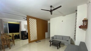A living room with a sofa, a coffee table, a TV, a ceiling fan, and a sliding door leading to a balcony. - Spacious 2BHK Mountain View | Near Palolem Beach (Canacona)